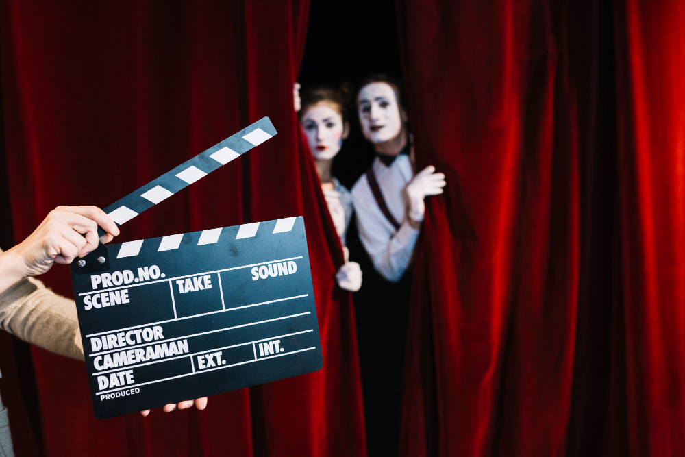 a person holding clapperboard in front of mime couple standing behind the red curtain
